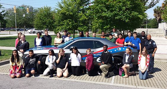 a group of kids around a police car taking a picture